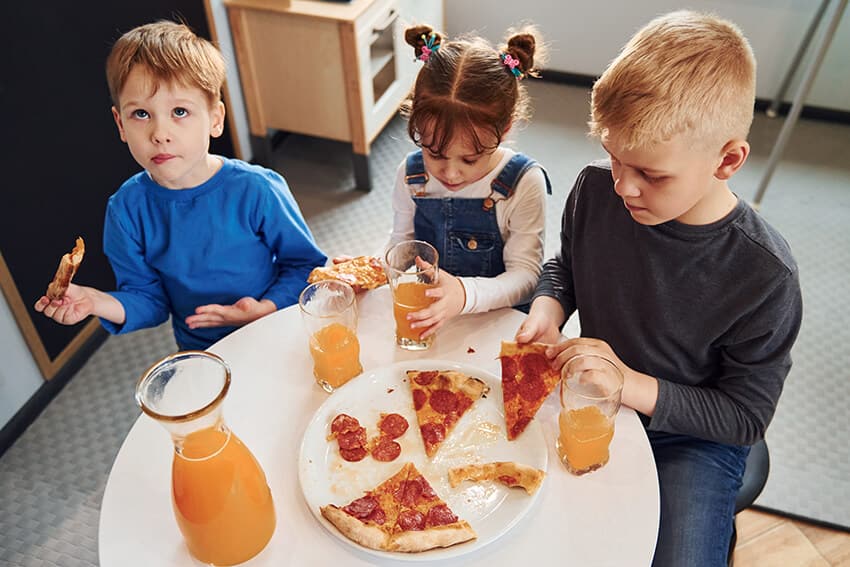 three-children-sitting-indoors-by-the-table-and-ea-6NE33KH.jpg